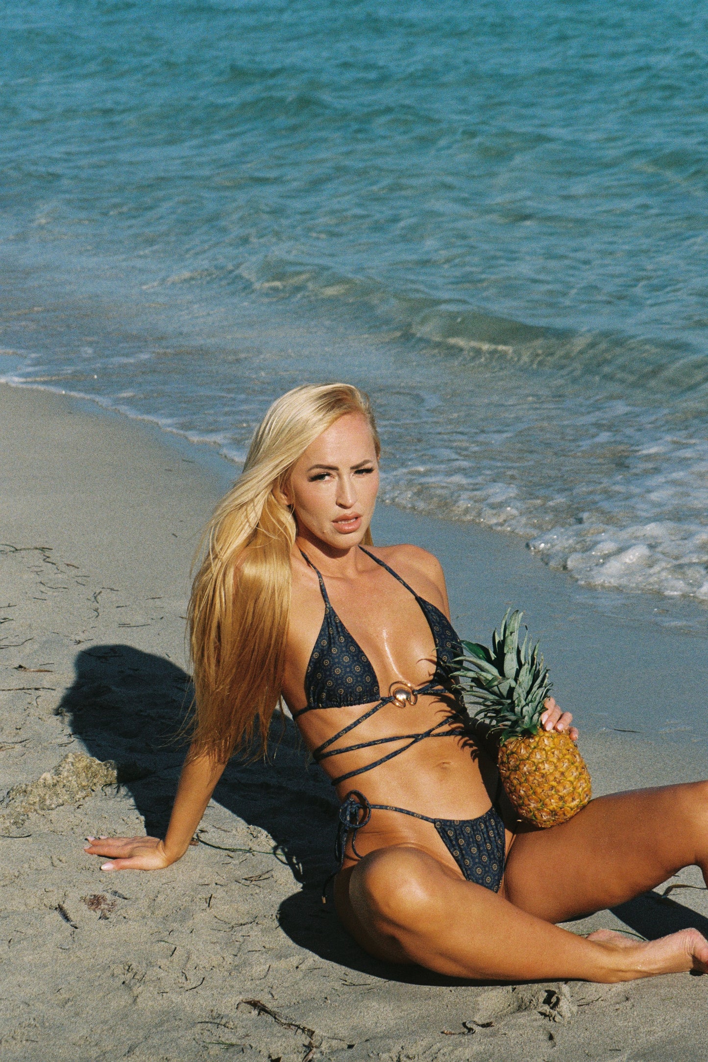 Woman in a bikini holding a pineapple on a beach